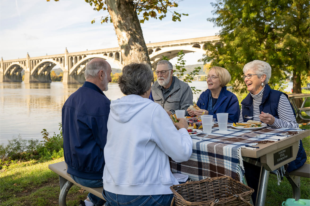 Residents have a picnic at a table by the water, showcasing the senior living culture of their community