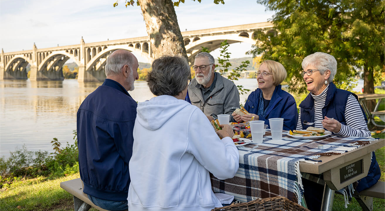 Residents have a picnic at a table by the water, showcasing the senior living culture of their community