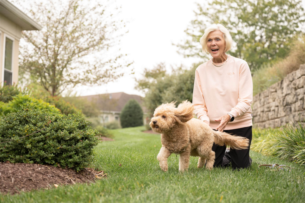 Woman and her dog playing in the grass as they tour a senior living community