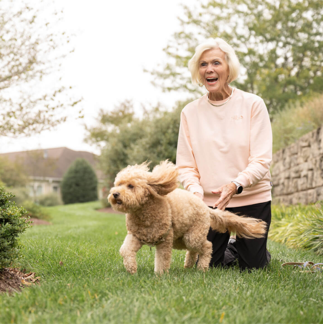 Woman and her dog playing in the grass as they tour a senior living community