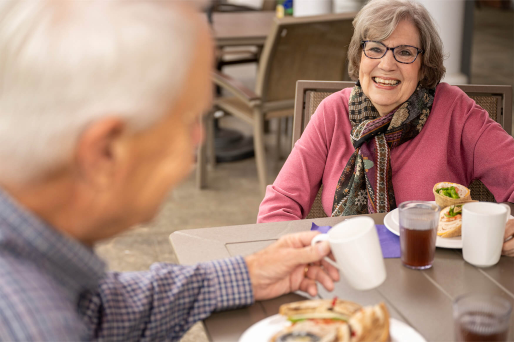 A senior couple eats outside at a retirement community, enjoying meal options for residents