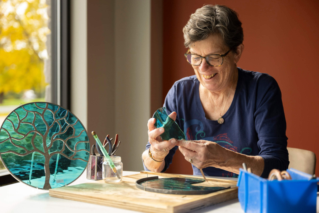 Woodcrest Villa resident smiles as she works on a stained glass project, showing how she is aging gracefully through her passions