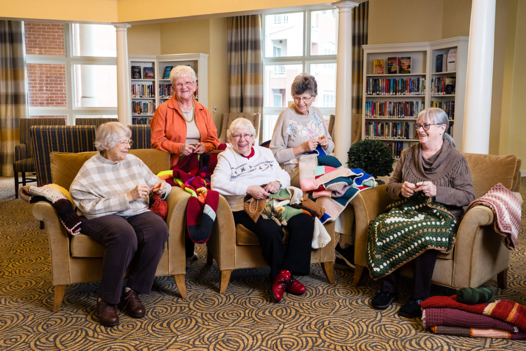 Five Woodcrest Villa residents sit in chairs and knit as they age gracefully with their passions.