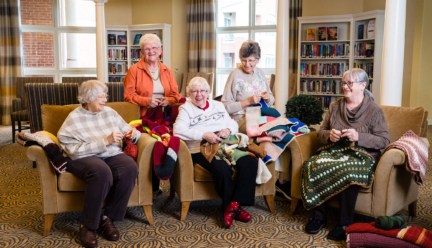 Five Woodcrest Villa residents sit in chairs and knit as they age gracefully with their passions.