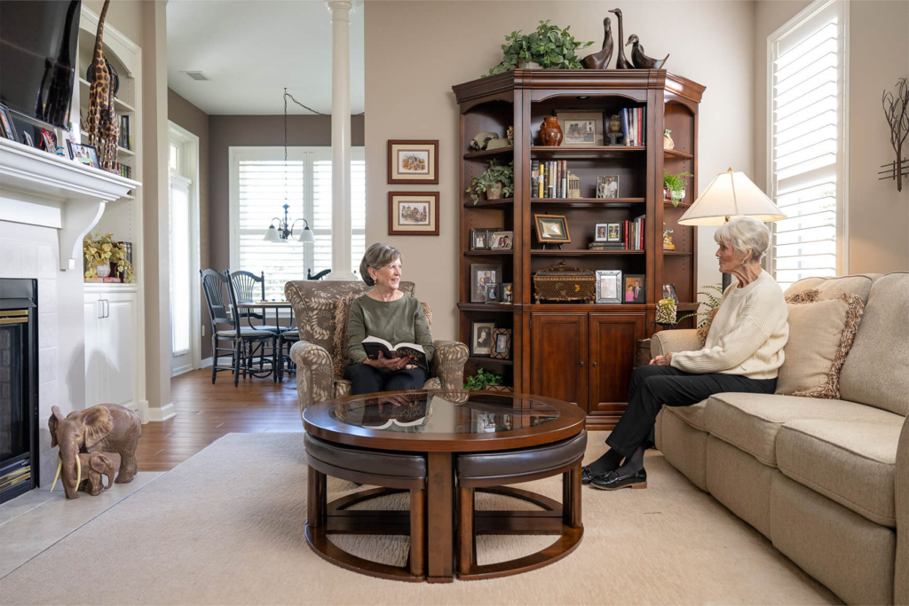 Two older women sit in a senior living apartment and chat