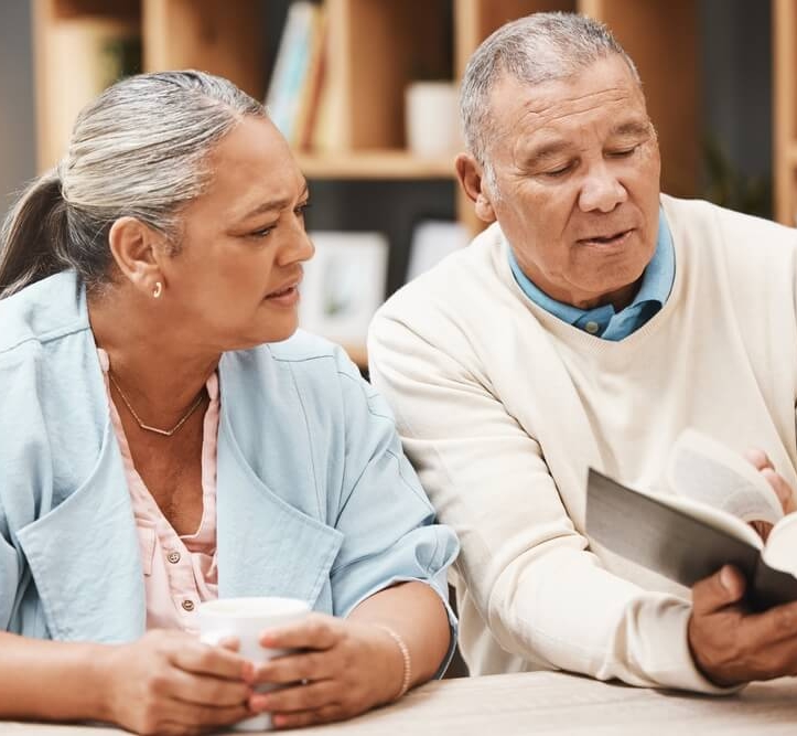 An older couple reads the Bible together while sitting at a table as part of Bloom Wellness at Woodcrest Villa