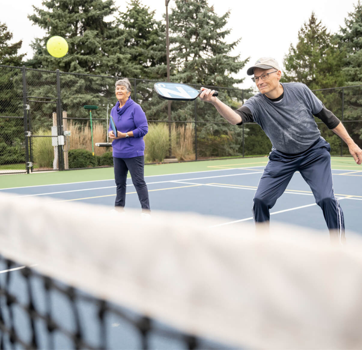Two senior living community residents play pickleball as part of Bloom Wellness at Woodcrest Villa