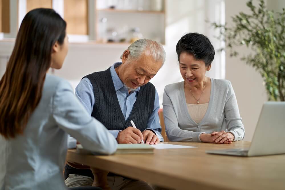 Couple signing a CCRC contract at a table with another woman watching