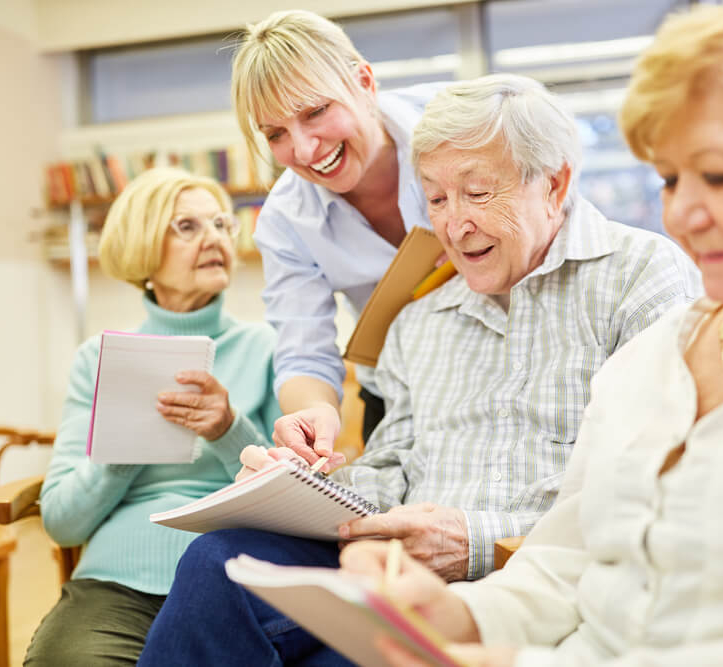 Four senior living community residents write in notebooks as part of a memoir writing program at Woodcrest Villa