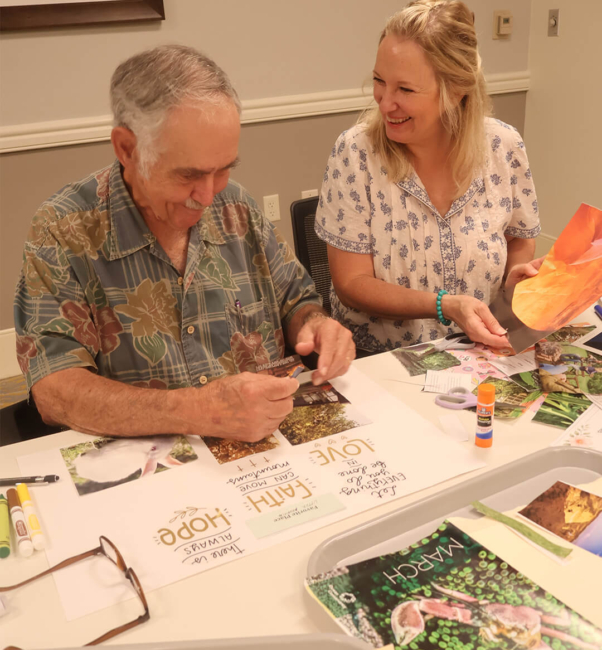 Caroline Kahler, the resident experience coordinator for Bloom Wellness Woodcrest Villa, sits at a table with an older man and helps him through a creative project