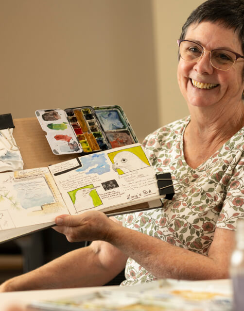 A resident of the Bloom Wellness Woodcrest Villa program holds up her watercolors and smiles