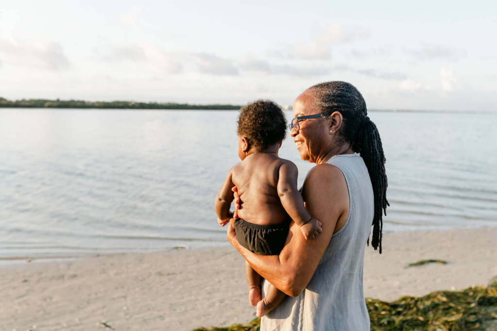 A resident of a retirement community in Lancaster County, PA holds her baby grandchild as she stands on the shore of a lake.