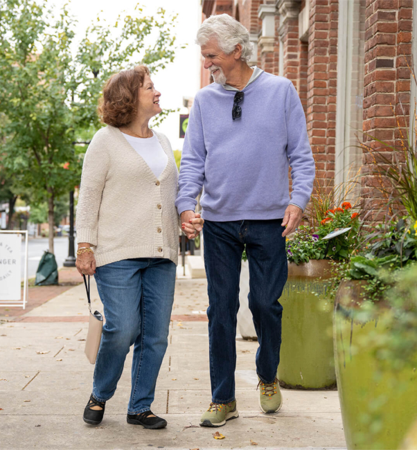 Two senior living residents walk down the sidewalk in Lancaster PA, holding hands and looking at each other